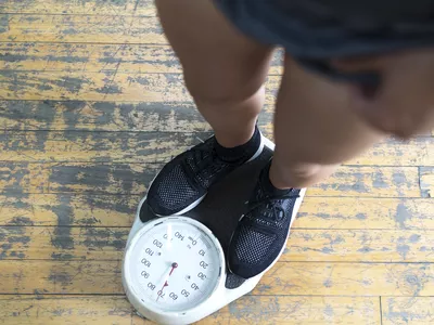 Low section of man checking weight on scale in gym