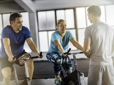 Overweight couple on exercise bikes talking with personal trainer