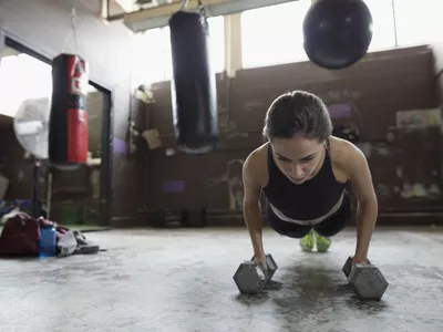 Strong female boxer doing plank exercise with dumbbells at gym