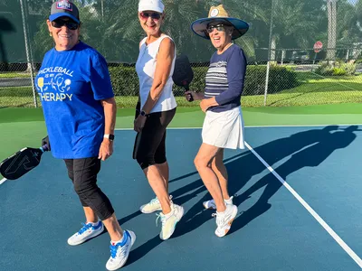 Three women holding pickleball paddles on a court smiling and posing together