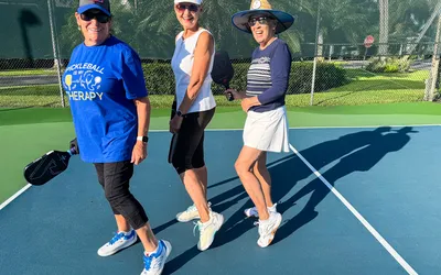 Three women holding pickleball paddles on a court smiling and posing together
