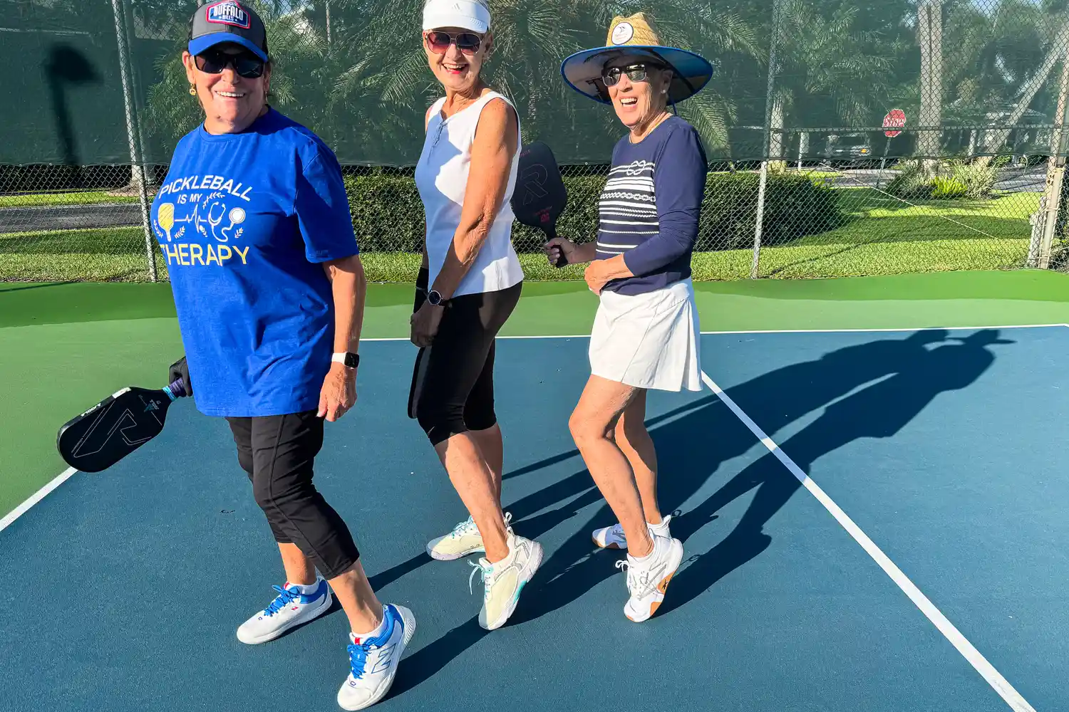 Three women holding pickleball paddles on a court smiling and posing together