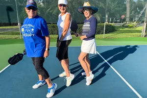 Three women holding pickleball paddles on a court smiling and posing together