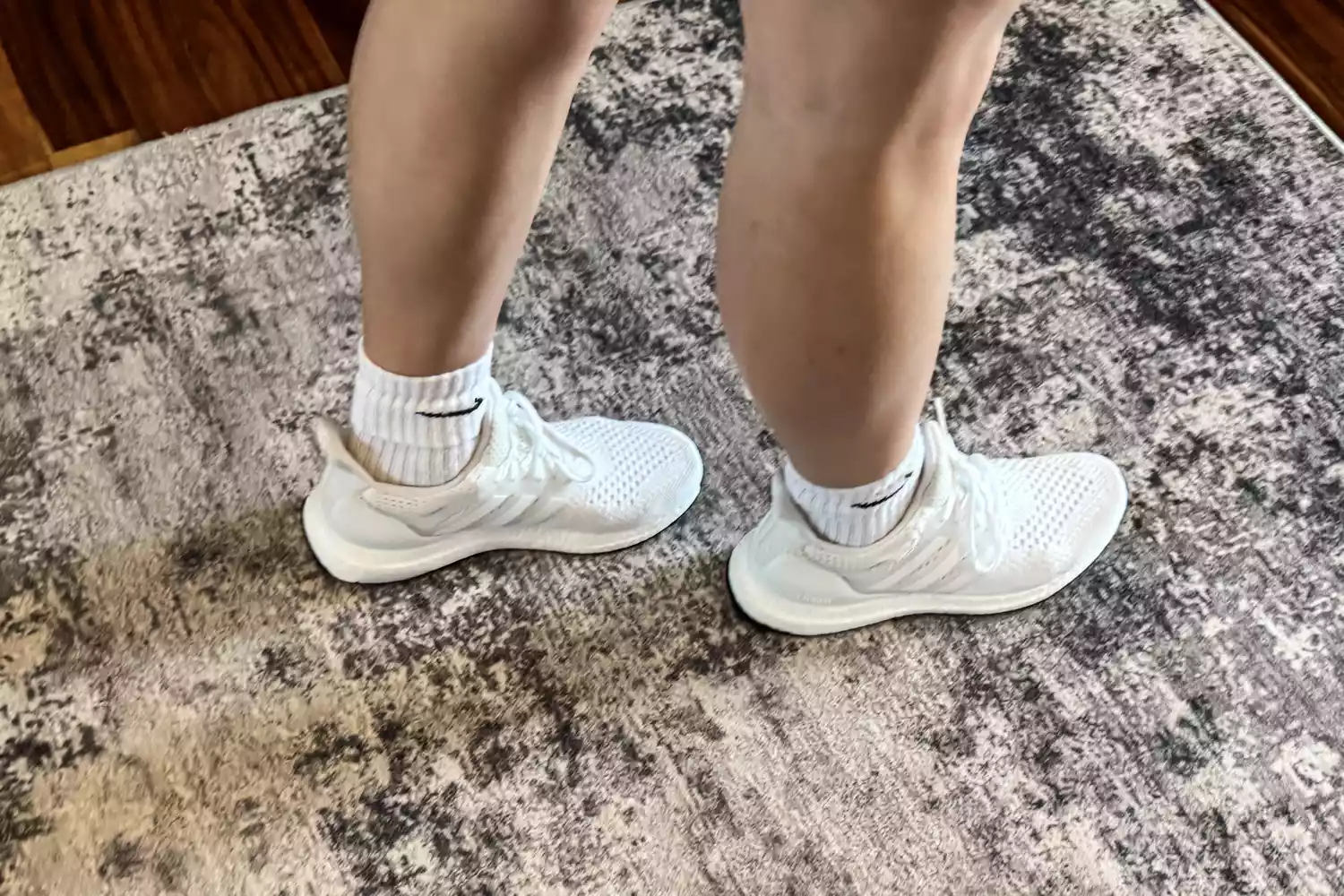 A close-up of two legs wering the Adidas Women's Ultraboost 1.0 Shoes on a rug