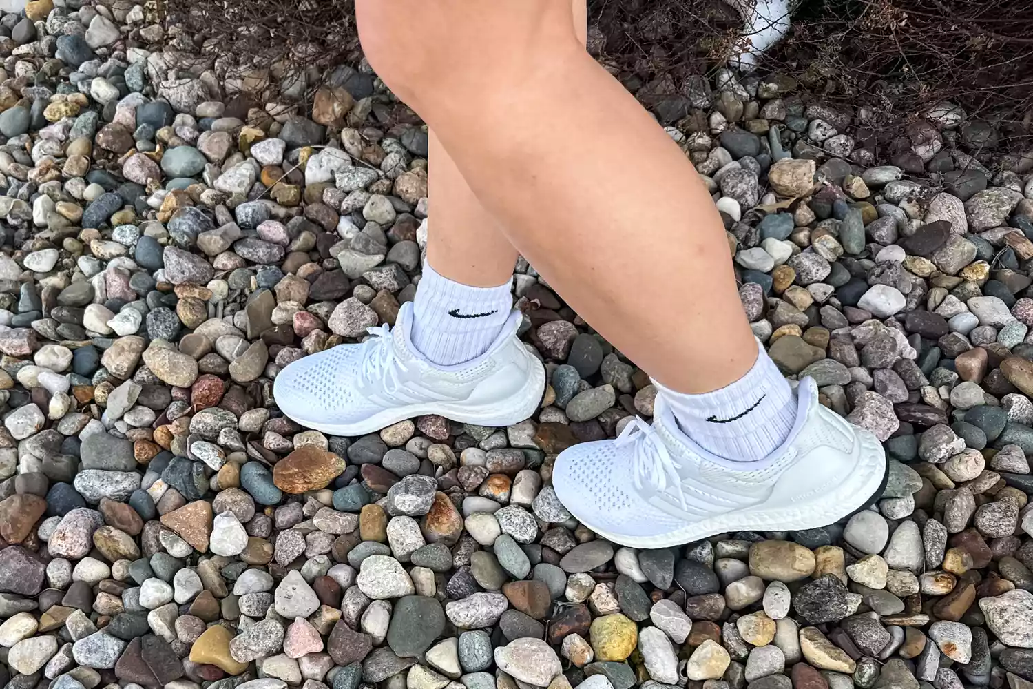 A close-up of two legs wearing the Adidas Women's Ultraboost 1.0 Shoes on stones