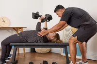 A person trains another person in lifting weights using the All in Motion 25 lb Adjustable Dumbbell