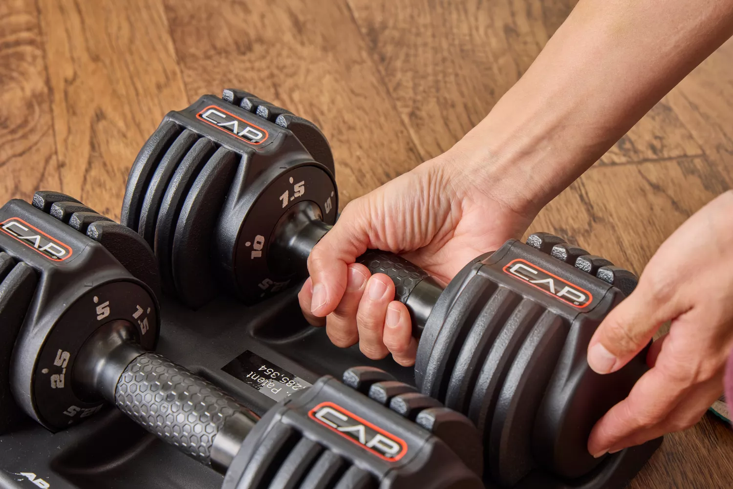 A person removes the CAP Barbell 25 lb. Adjustable Dumbbell from the base