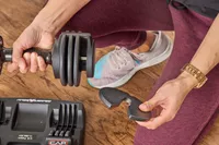 A person adds weight to the CAP Barbell 25 lb. Adjustable Dumbbell