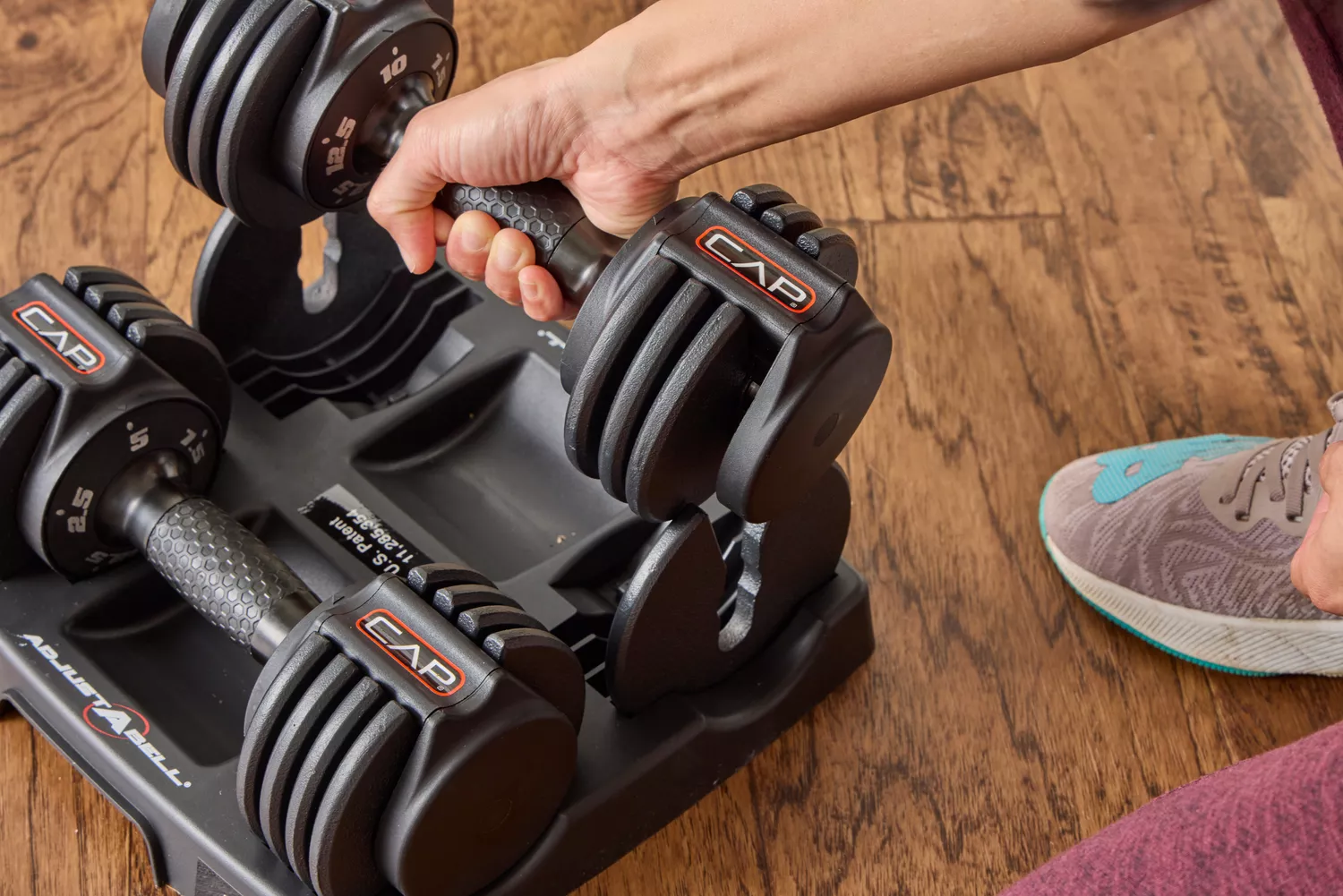 A person removes the CAP Barbell 25 lb. Adjustable Dumbbell from the base