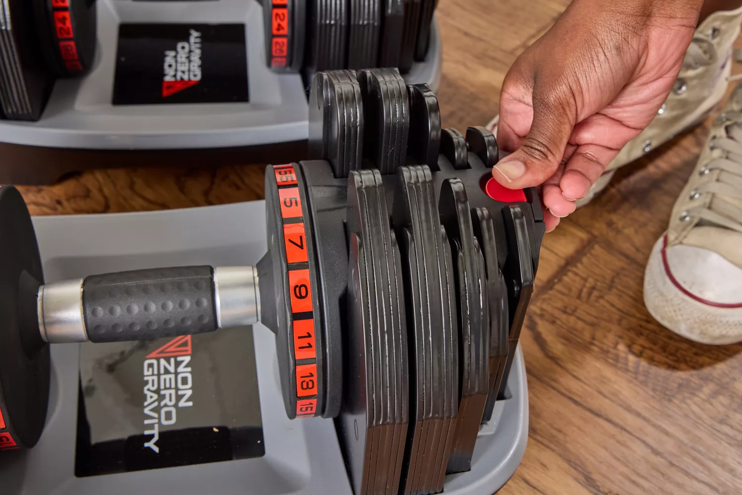 A person presses a button on the Non Zero Gravity 55 lbs PowerDyne Adjustable Dumbbell base