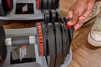 A person presses a button on the Non Zero Gravity 55 lbs PowerDyne Adjustable Dumbbell base