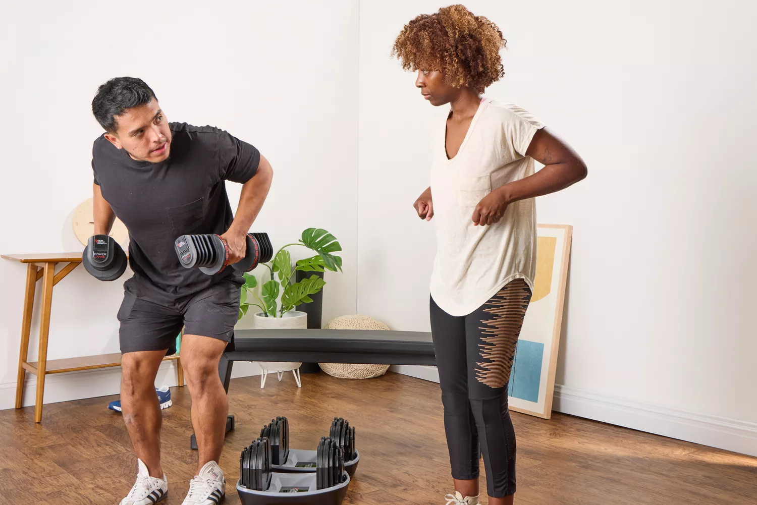 A person instructs another person on how to lift the Non Zero Gravity 55 lbs PowerDyne Adjustable Dumbbells