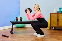 A person does a deep squat while hold a BCBIG Adjustable Dumbbell