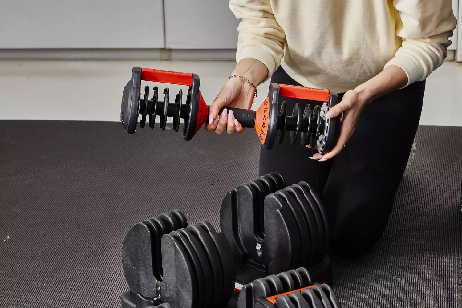 Hand holding FitRx SmartBells Set Quick Select Adjustable Dumbbells and kneeling in front of stand