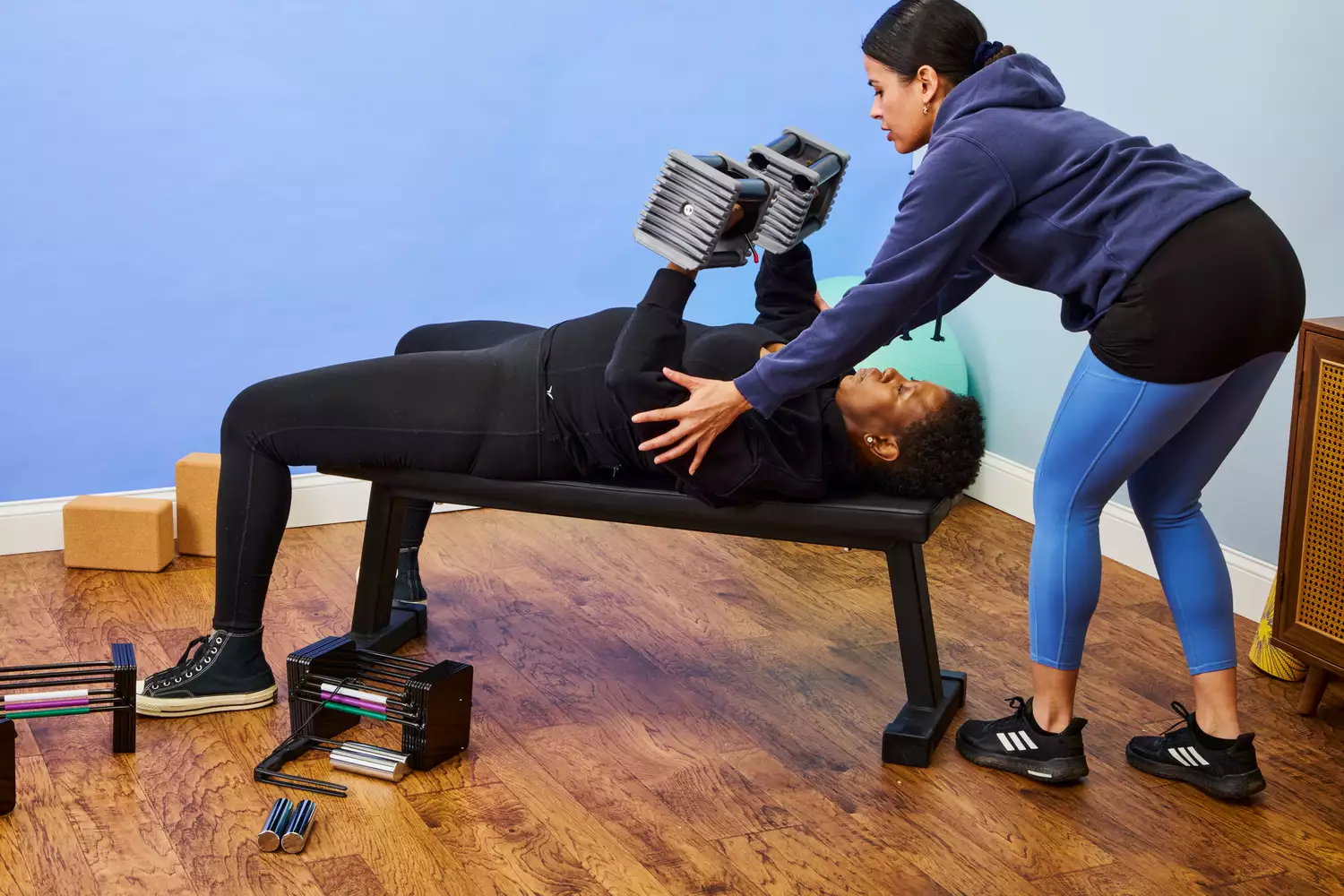 A person spots another person lifting the POWERBLOCK Elite EXP Adjustable Dumbbells on a weight bench