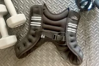 Aduro Sport Adjustable Weighted Vest placed on a textured mat surrounded by gym equipment including dumbbells and an ab wheel