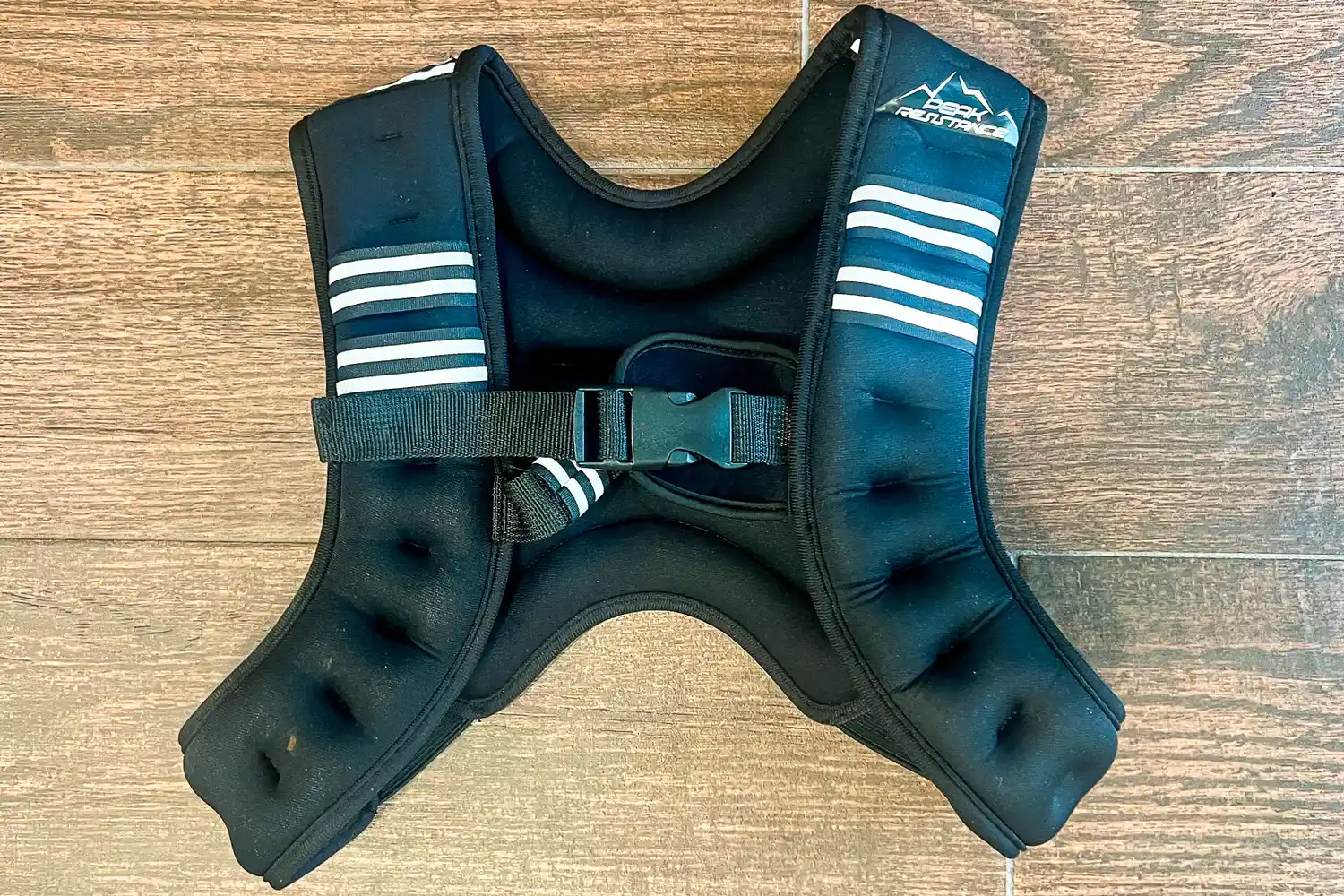 Aduro Sport Adjustable Weighted Vest with adjustable straps lying on a wooden floor