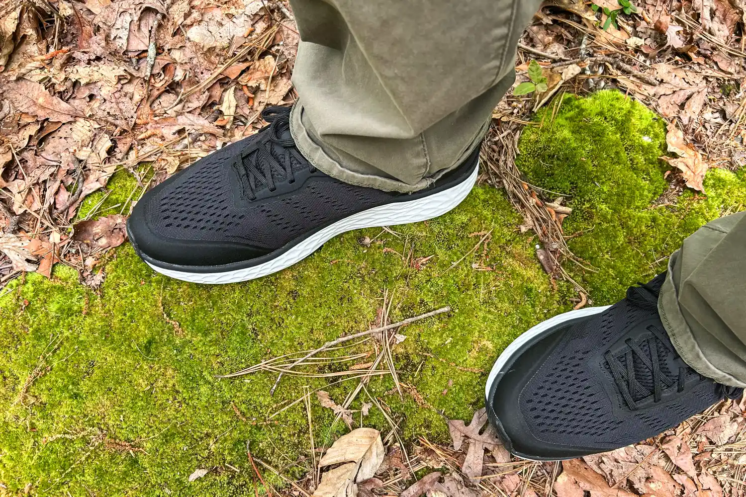 A view of feet wearing Aetrex Chase Arch Support Sneakers on moss-covered ground with dried leaves