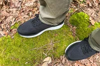A view of feet wearing Aetrex Chase Arch Support Sneakers on moss-covered ground with dried leaves