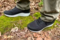 A person wearing Aetrex Chase Arch Support Sneakers standing on moss in a forest setting