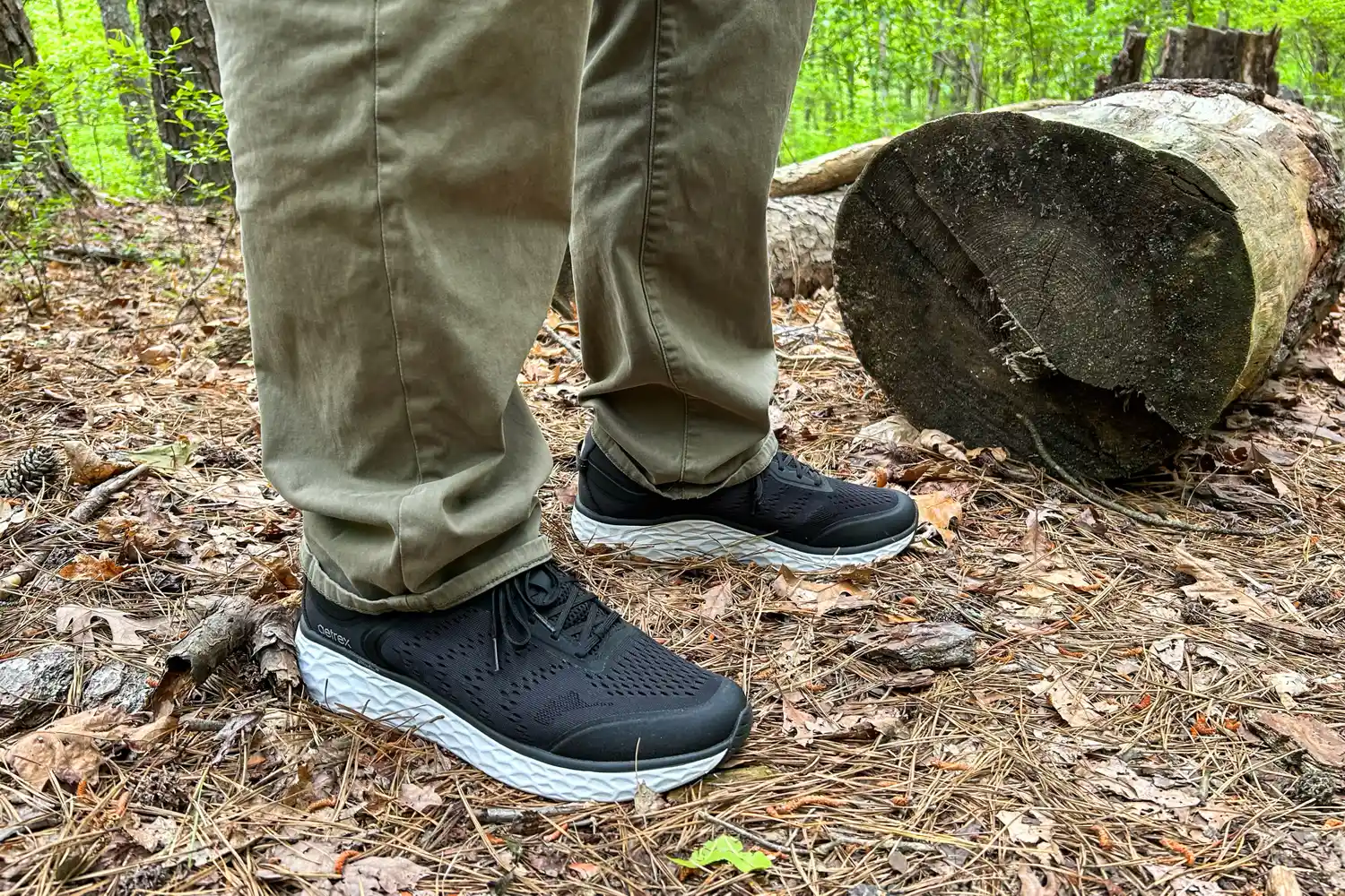 A person wearing Aetrex Chase Arch Support Sneakers standing near a log in a forest setting