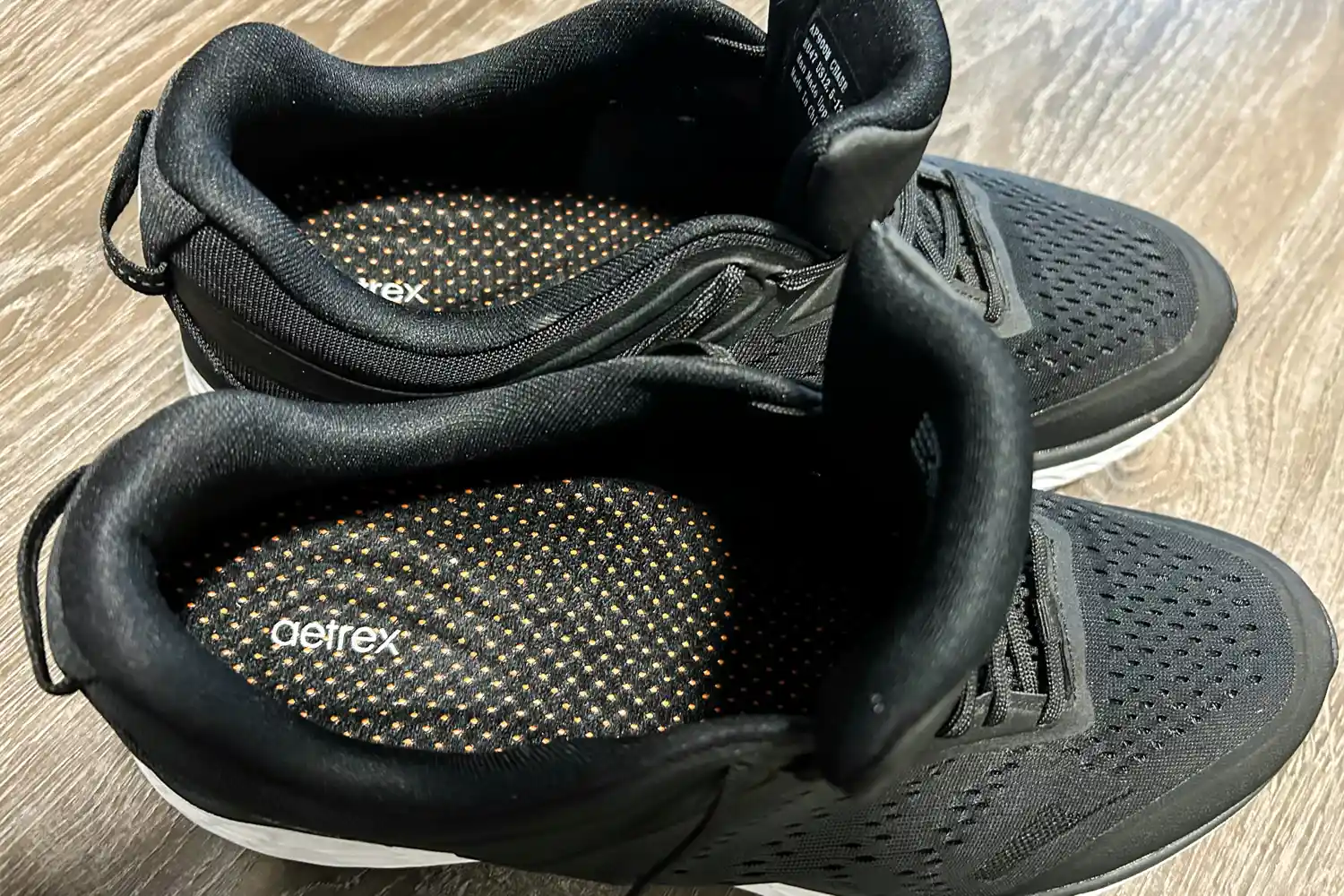 A pair of Aetrex Chase Arch Support Sneakers on a smooth wooden surface
