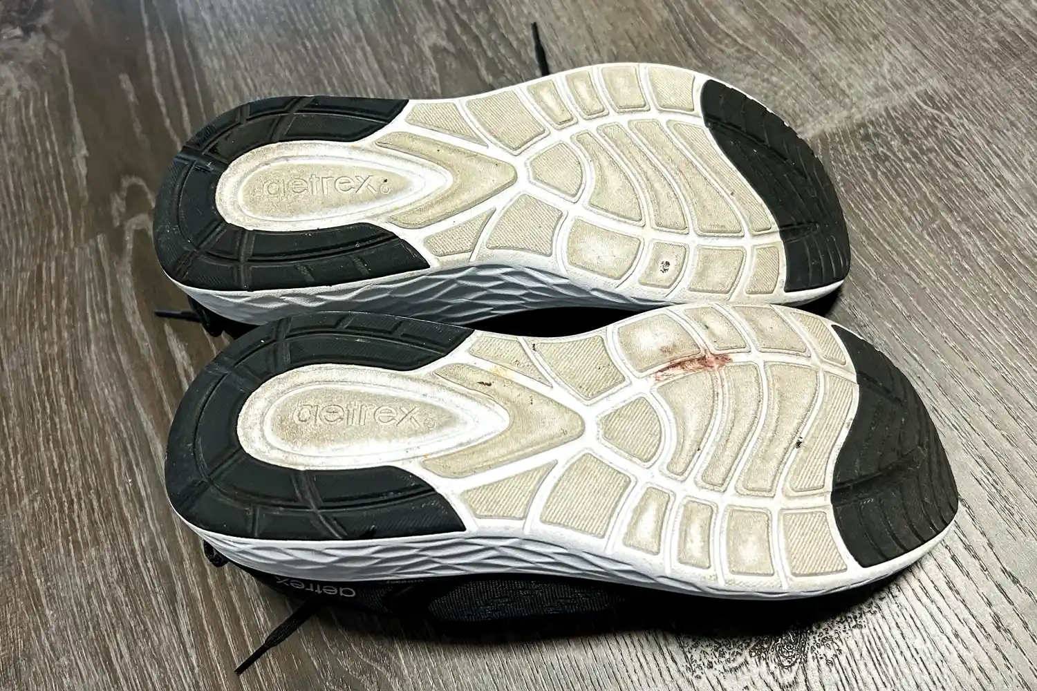 A pair of Aetrex Chase Arch Support Sneakers placed upside down showing the soles on a wooden floor