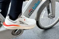 A person pedals a bicycle wearing the Altra Men's Paradigm 7 Sneakers