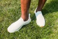 A person wears the APL Men's TechLoom Travelers while standing in grass