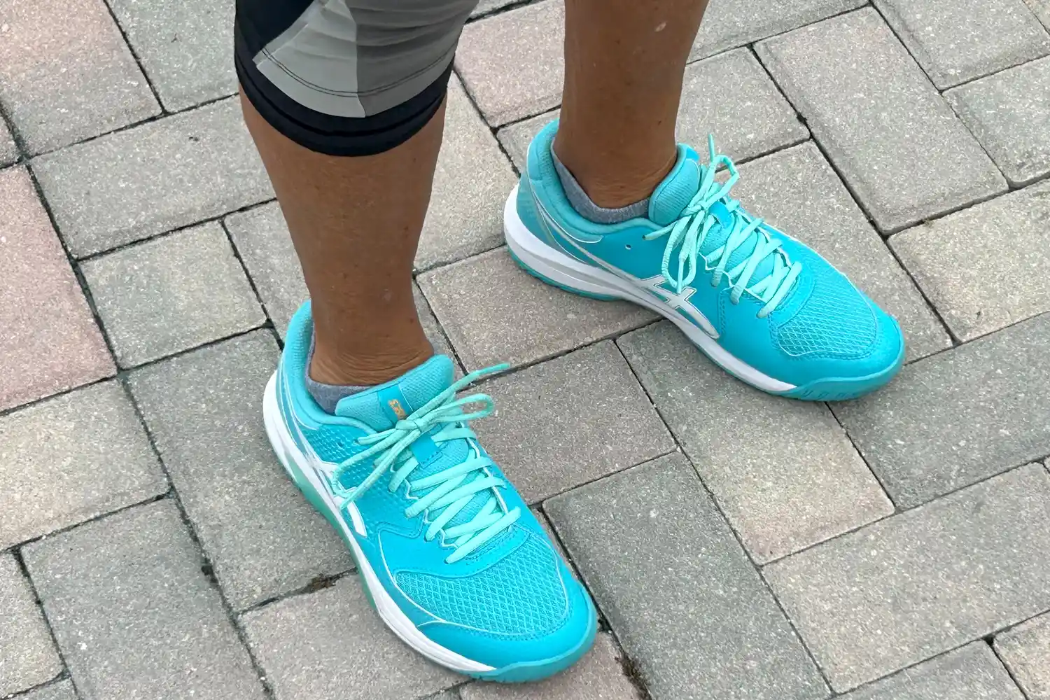 A person wears the Asics Women's Gel-Dedicate 8 Pickleball Shoes while standing on bricks