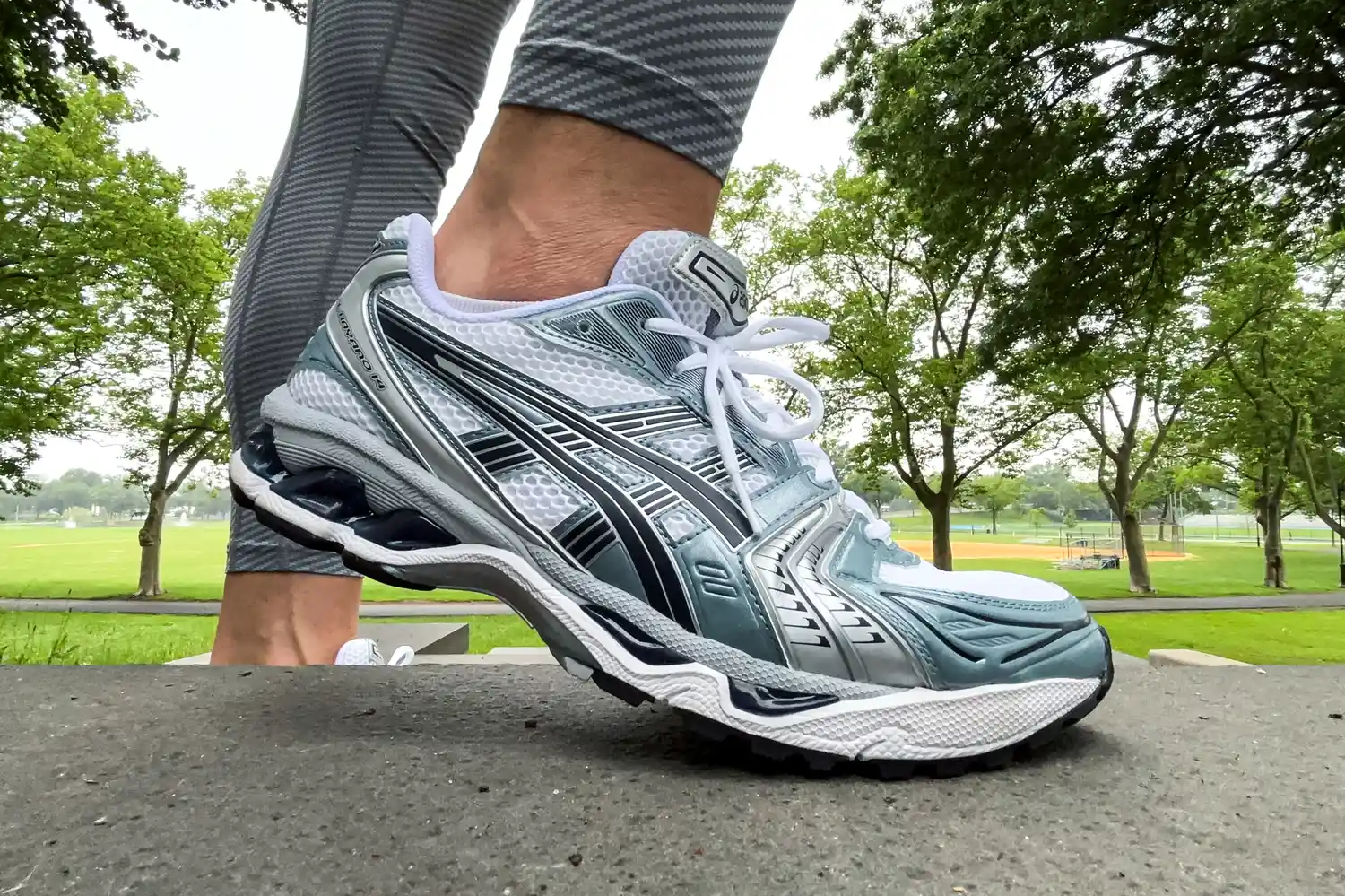 A person stands on a stone step while wearing the Asics Men's Gel-Kayano 14 Sneakers