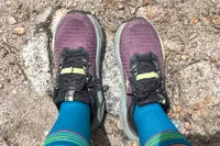 A person wearing Asics Women's Gel-Trabuco 13 Trail Running Sneakers and blue socks standing on rocky terrain
