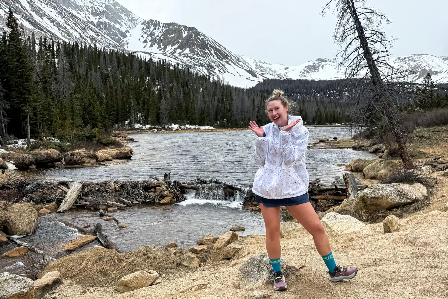 A person smiles and poses near a river wearing the Asics Women's Gel-Trabuco 13 Trail Running Sneakers