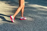 A close-up of two legs walking on black top while wearing Brooks Hyperion Tempo Road-Running Shoes