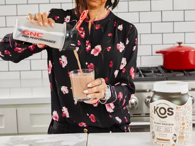 A person pouring KOS Vegan superfood into a glass