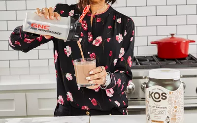 A person pouring KOS Vegan superfood into a glass