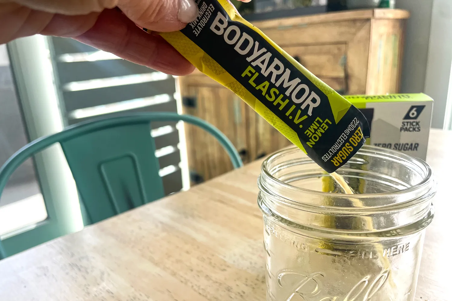 A hand pours BodyArmor Flash IV powder into a glass jar