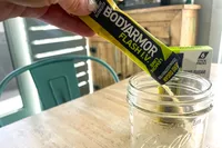 A hand pours BodyArmor Flash IV powder into a glass jar