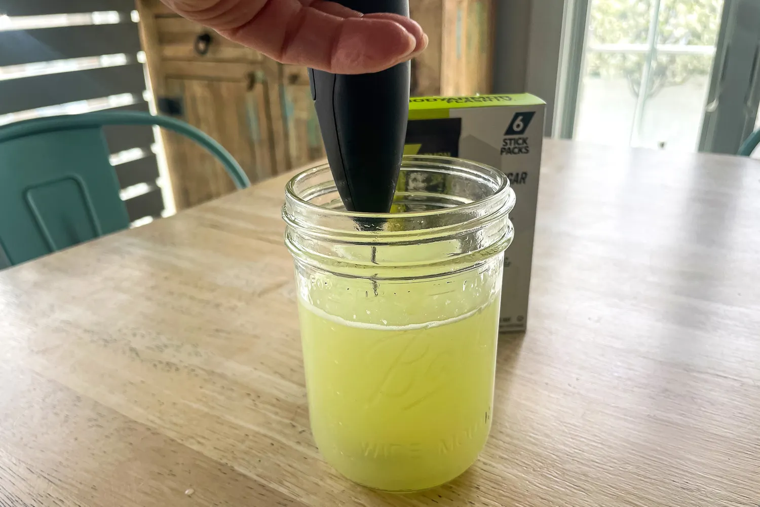 Hand using a device to mix liquid in a glass jar a product box in the background