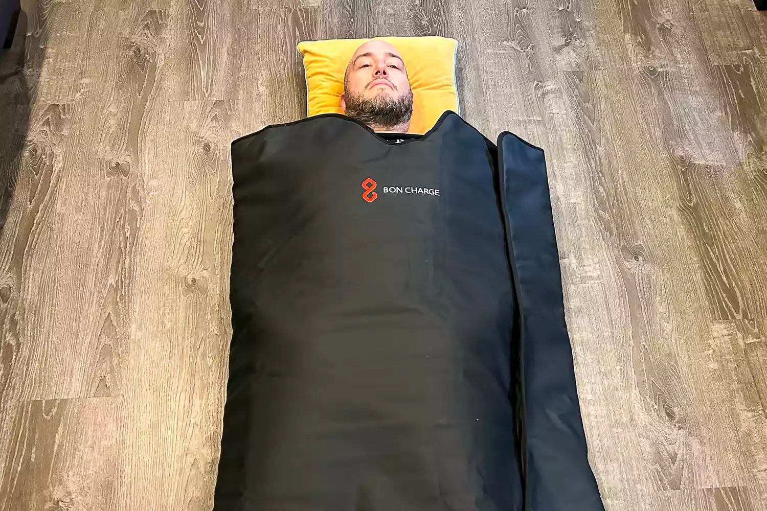 A person laying in the Bon Charge Infrared Sauna Blanket placed in a wooden floor