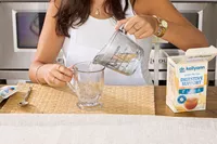A person adds water and Dr. Kellyann Bone Broth + Digestive Support to a glass