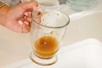 A person holds up a glass of Dr. Kellyann Bone Broth + Digestive Support