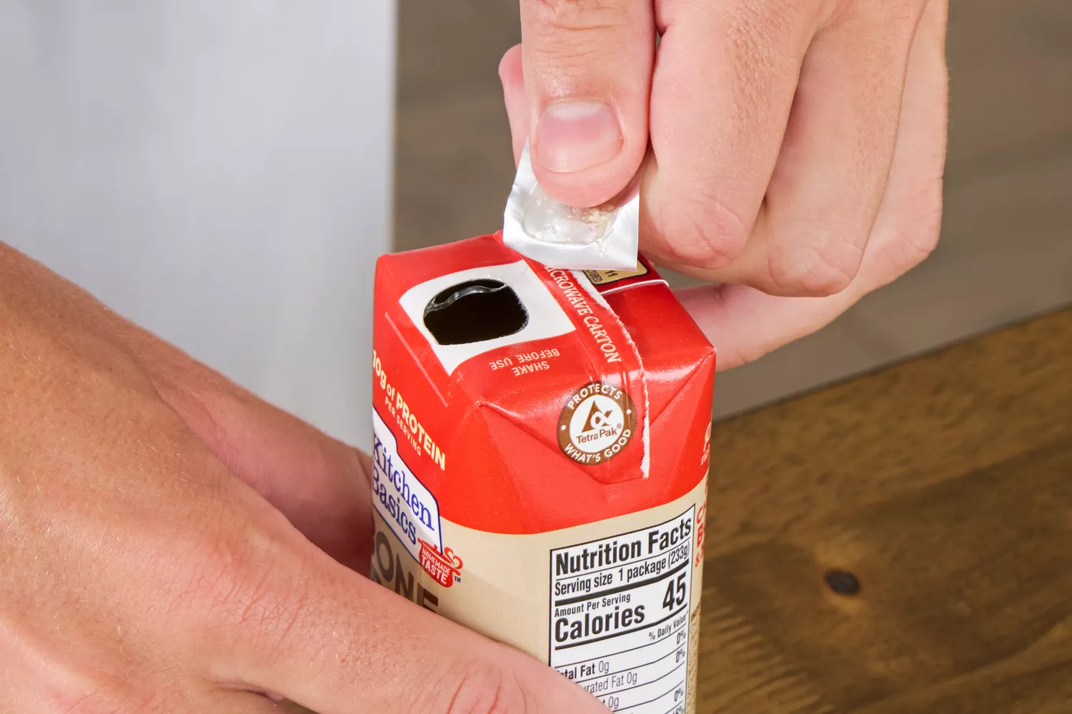 A person removes the cover on the Kitchen Basics Turmeric & Ginger With Lemongrass Chicken Bone Broth