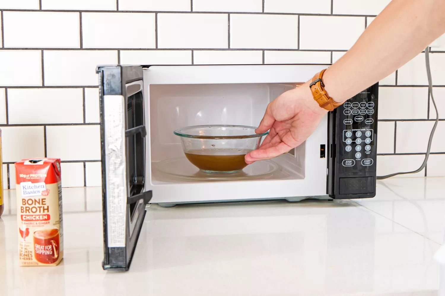 A person places a bowl of Kitchen Basics Turmeric & Ginger With Lemongrass Chicken Bone Broth into a microwave