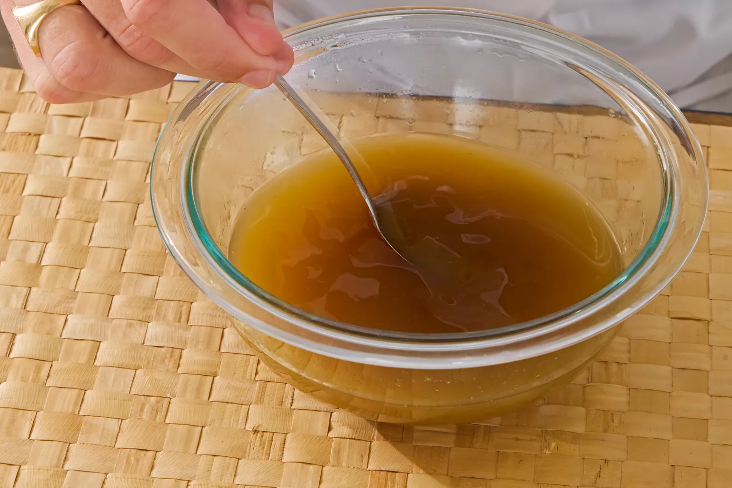 A person stirs Kitchen Basics Turmeric & Ginger With Lemongrass Chicken Bone Broth in a glass bowl