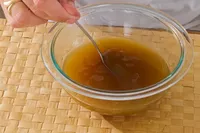 A person stirs Kitchen Basics Turmeric & Ginger With Lemongrass Chicken Bone Broth in a glass bowl