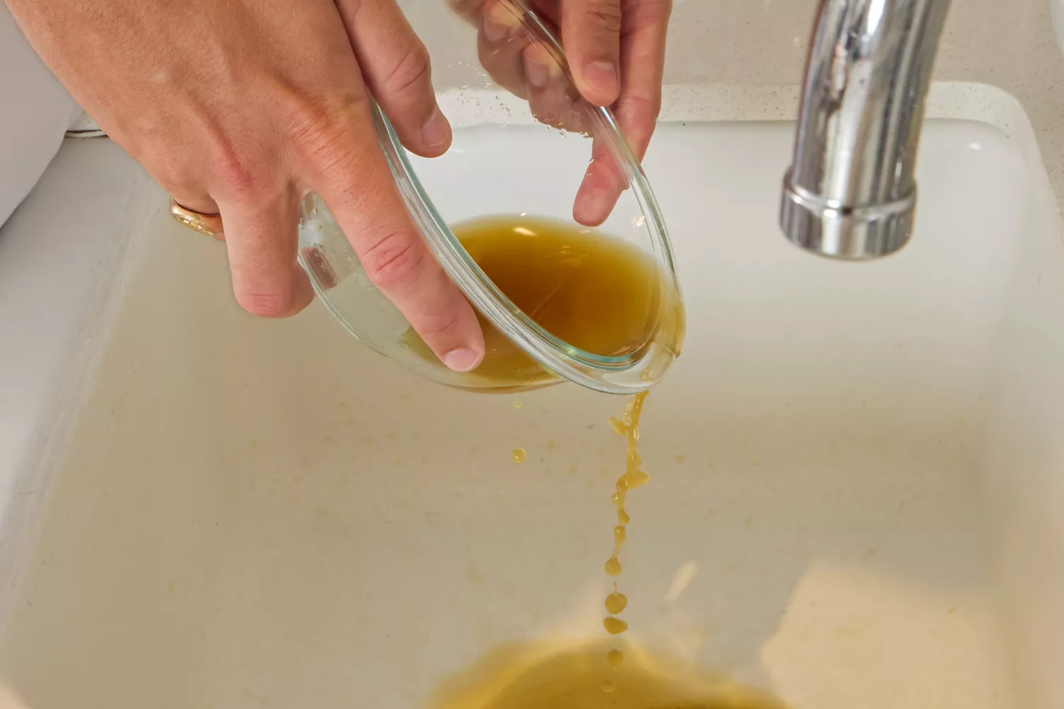 A person pours Kitchen Basics Turmeric & Ginger With Lemongrass Chicken Bone Broth into a sink