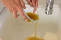 A person pours Kitchen Basics Turmeric & Ginger With Lemongrass Chicken Bone Broth into a sink