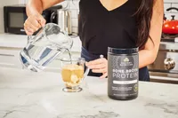 A person pours water into Ancient Nutrition Bone Broth Protein powder