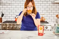 A person sips a glass of Brodo Hearth Bone Broth in kitchen